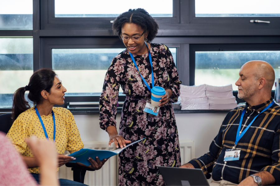 Educators meeting and discussing. One person is holding a coffee cup and another is holding a binder of material that they are pointing too.
