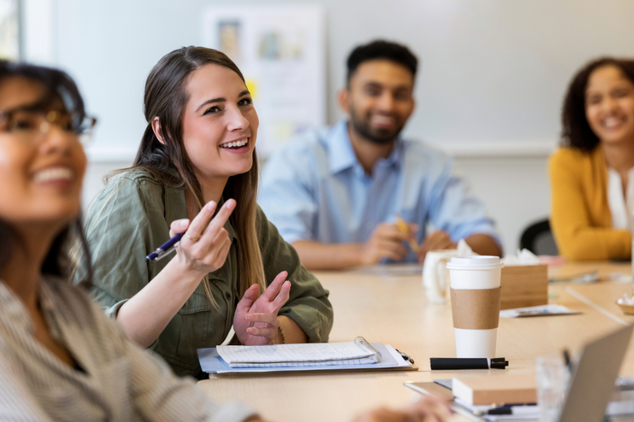Photo of adults seated at a conference table smiling with one adult gesturing with her hand. 